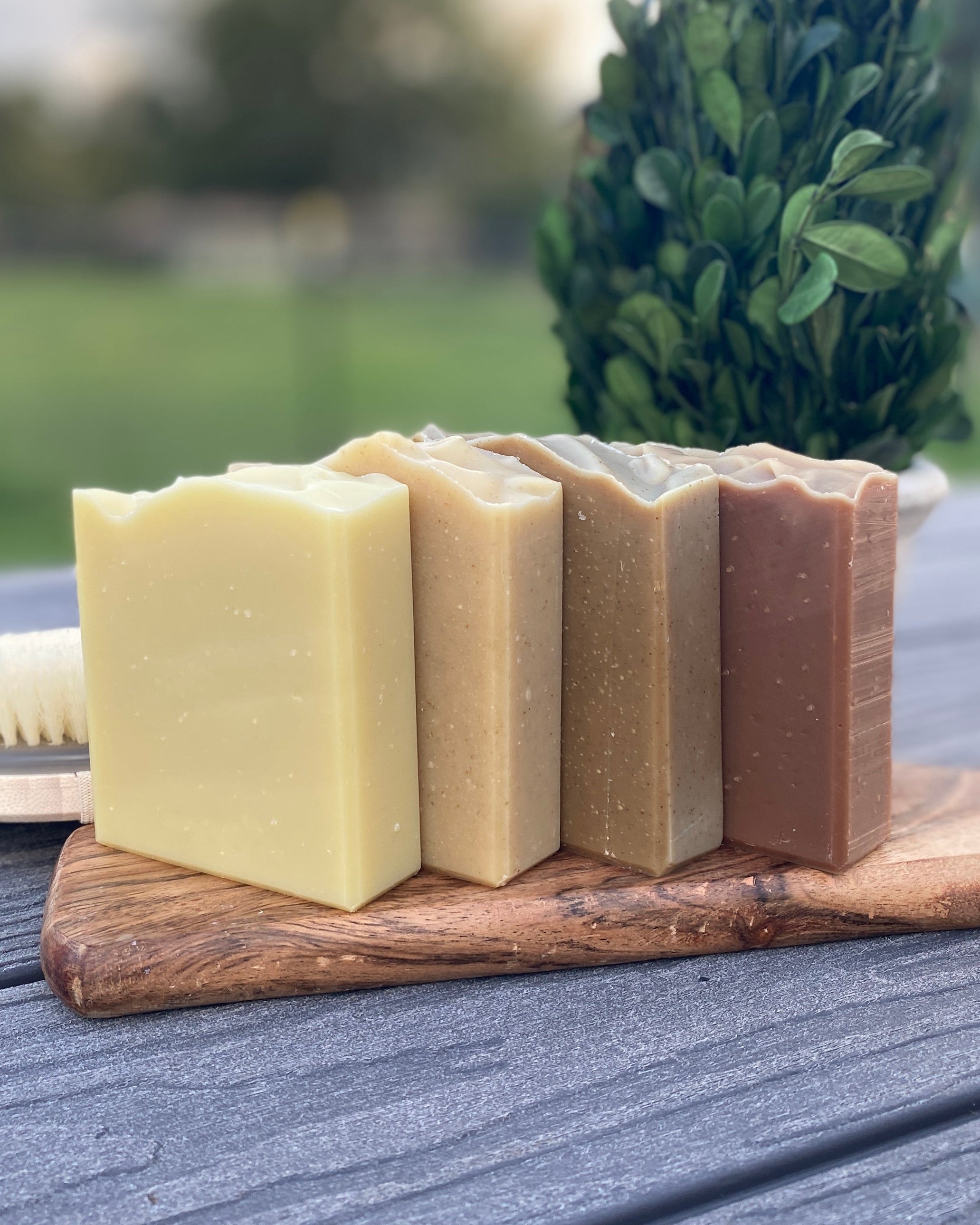 A collection of 4 fragrance free, plant based bars of handmade soap sitting on a wooden board in a natural setting